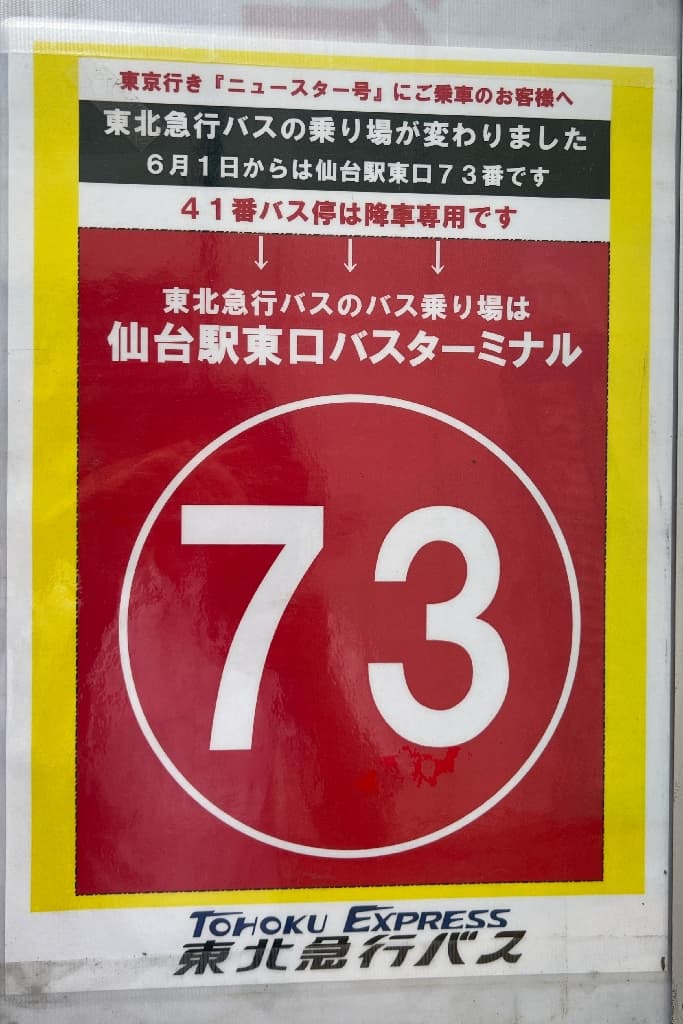 Ultra-realistic high-quality photograph of a notice for the New Star bus, featuring a large, prominent white number 73 inside a striking red circle, indicating the new boarding location at the Sendai Station East Exit. 東京行き「ニュースター号」の新しい乗り場を示す案内板。赤い大きな円の中に白抜きで「73」という数字が力強く強調されており、仙台駅東口バスターミナルへの変更がひと目で理解できるデザイン